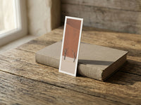 Terracotta fine art bookmark resting on a linen-bound book in soft window light